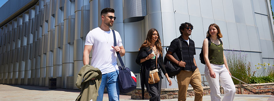 Four students walk in the sun next to a shining modern building on Bristol’s campus