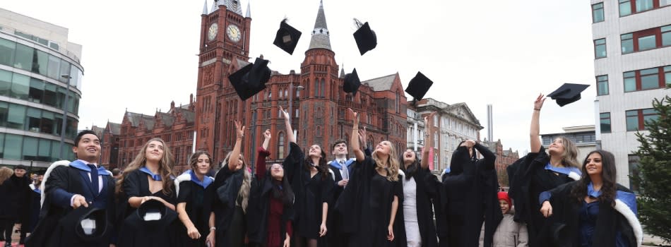A group of graduates celebrating by throwing their mortarboard hats into the air.
