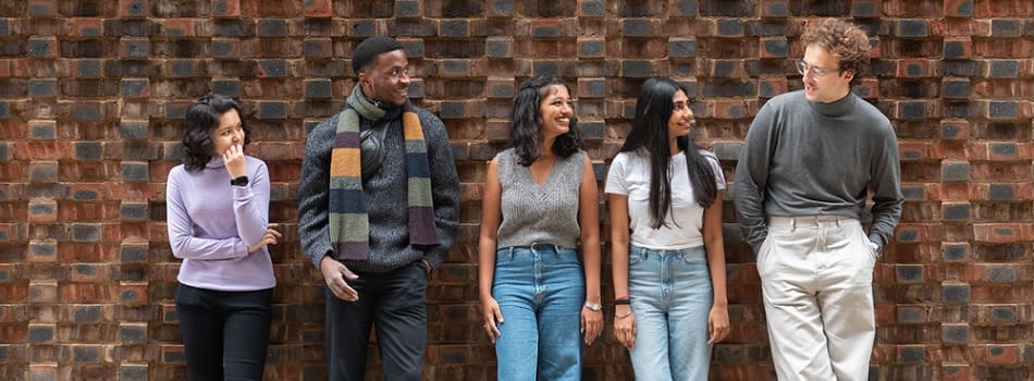5 students leaning against a wall, chatting