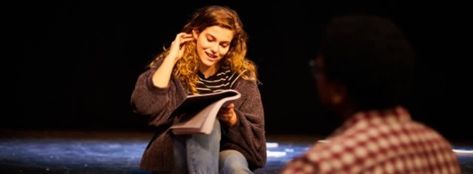 A person sitting on a stage, reading.