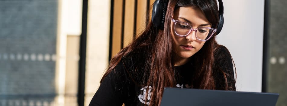 Girl sits with headphones looking at a laptop