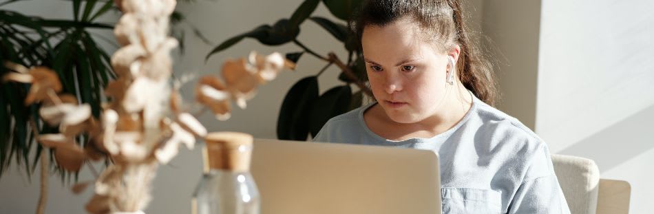 Woman sat at table with laptop on lap and headphones in