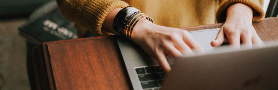Person typing on keyboard in orange jumper and bracelets