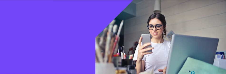 A female looking at her phone whilst sat in front of a computer