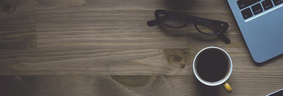 Wooden table top with laptop, sunglasses and coffee cup