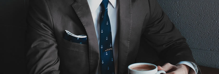 Torso of person in suit and tie, holding a coffee cup.