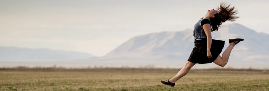 Woman running and jumping on field, against mountain backdrop