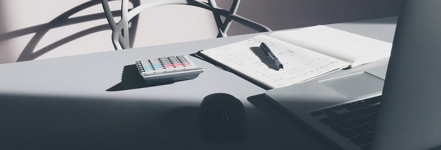 Desk with calculator, pen and paper, and laptop
