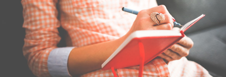 Close up of women in an orange check dress writing in a red notebook Close up of women in an orange check dress writing in a red notebook