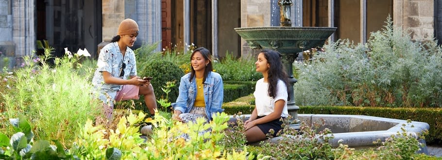 Three students sitting around a fountain in a garden