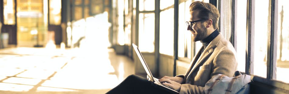 Guy sat down with laptop on lap smiling