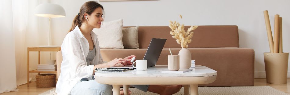Woman sitting on floor of living room with laptop on coffee table